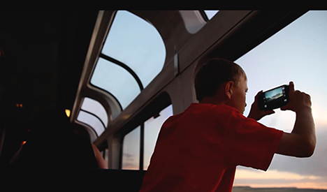 Young boy takes photo of sunset on his phone while riding a train